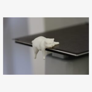 Cream 3D printed sleepy cat shelf-edge figure on a laptop edge
