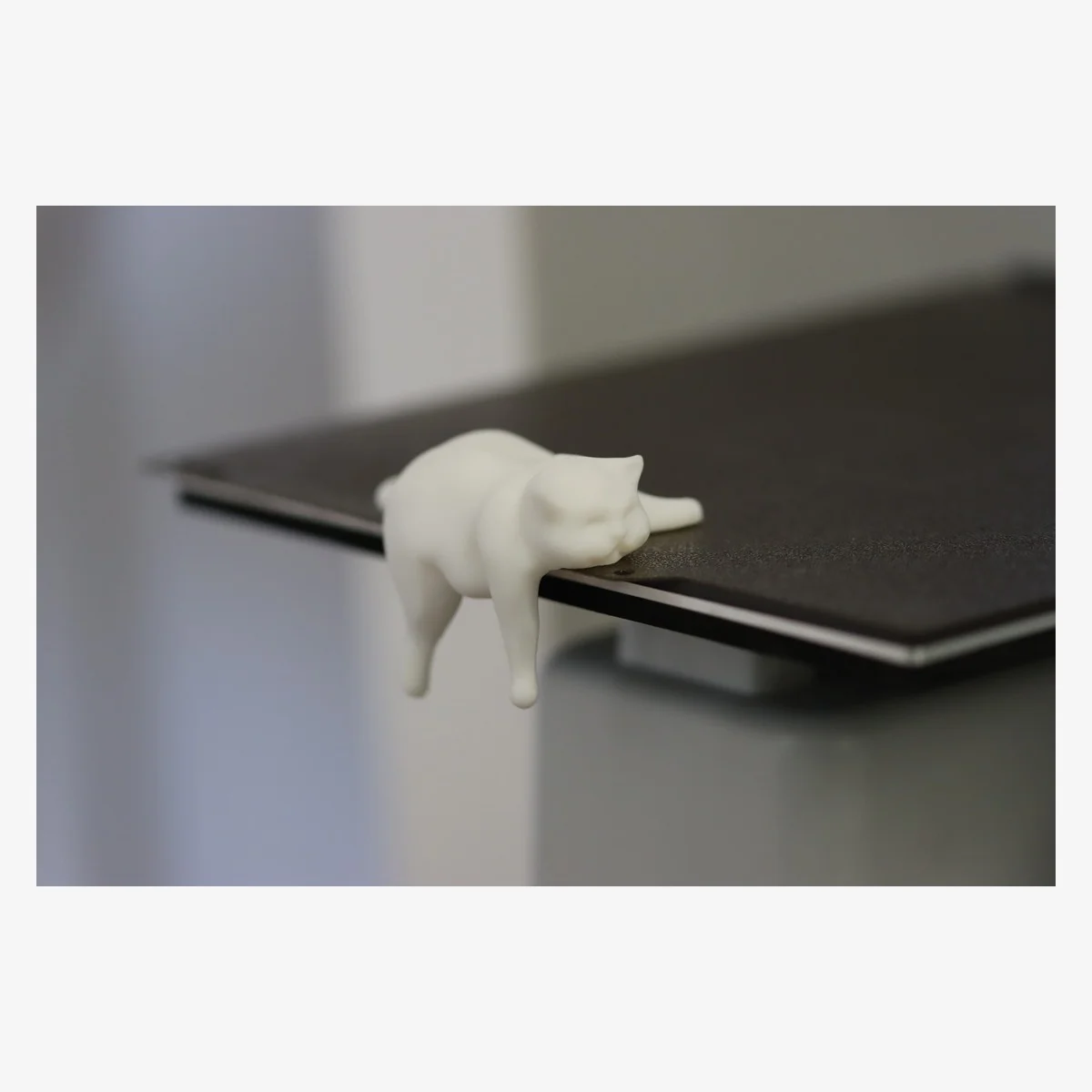 Cream 3D printed sleepy cat shelf-edge figure on a laptop edge
